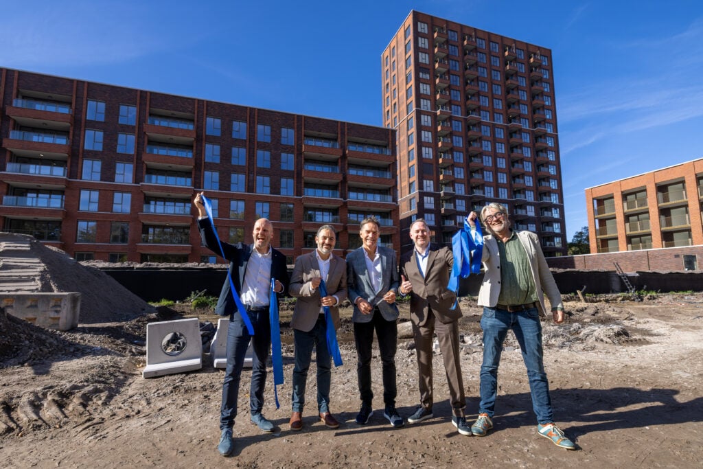 Foto van 5 bestuurders met op de achtergrond het nieuwbouwproject